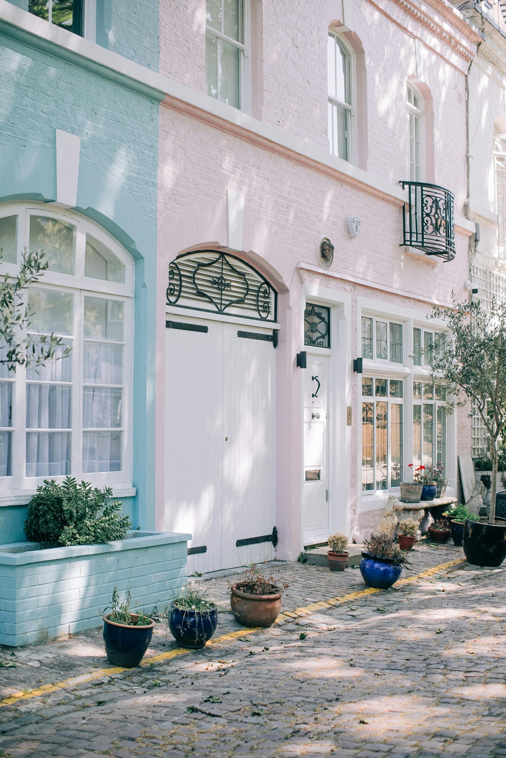 Beautiful pastel-colored mews houses with potted plants on cobblestone street.